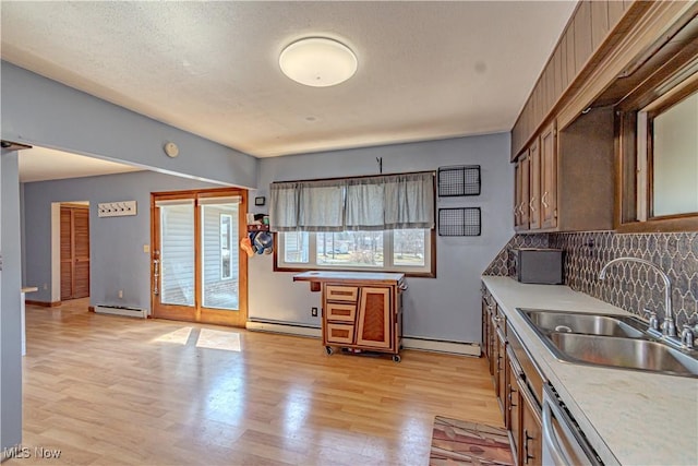 kitchen with a sink, light wood-style floors, baseboard heating, and decorative backsplash