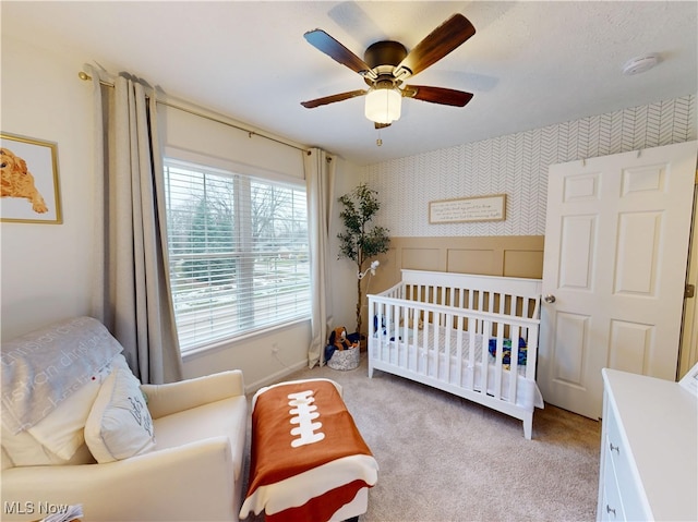 bedroom featuring a crib, light colored carpet, ceiling fan, and wallpapered walls