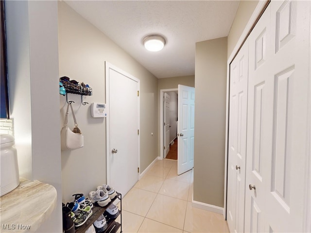 corridor featuring light tile patterned floors, a textured ceiling, and baseboards