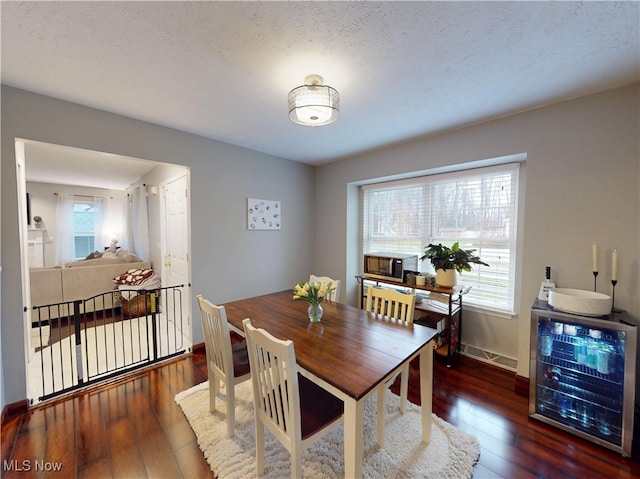 dining space with baseboards, wine cooler, a textured ceiling, and hardwood / wood-style flooring