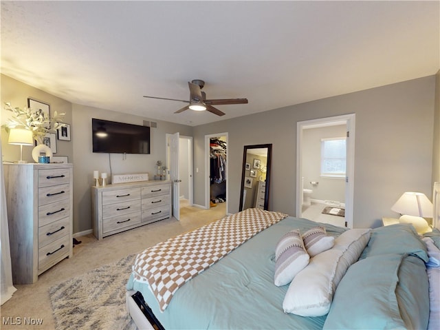 bedroom with connected bathroom, a walk in closet, ceiling fan, light colored carpet, and a closet