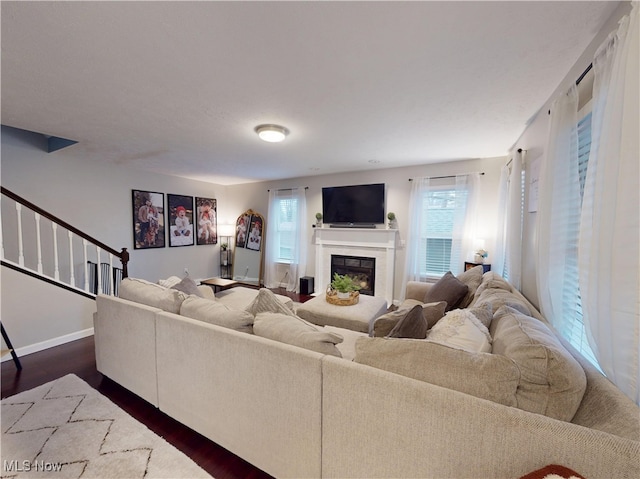 living area featuring a glass covered fireplace, stairs, dark wood-type flooring, and baseboards