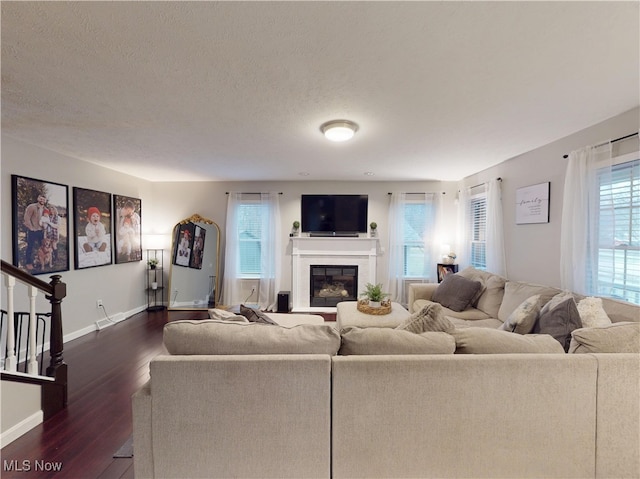 living area featuring dark wood-style floors, a glass covered fireplace, a healthy amount of sunlight, and a textured ceiling