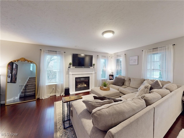 living room with a textured ceiling, a glass covered fireplace, hardwood / wood-style floors, stairway, and baseboards