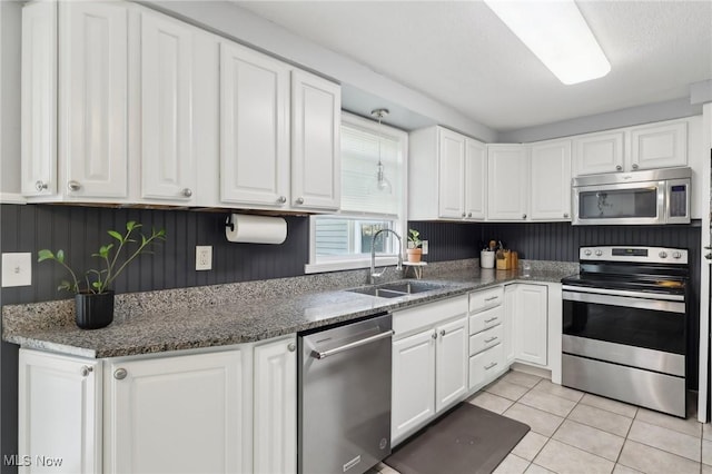 kitchen with light tile patterned floors, dark stone counters, a sink, stainless steel appliances, and white cabinetry