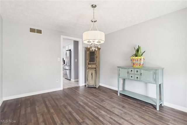 unfurnished dining area with visible vents, baseboards, a chandelier, and dark wood-style flooring