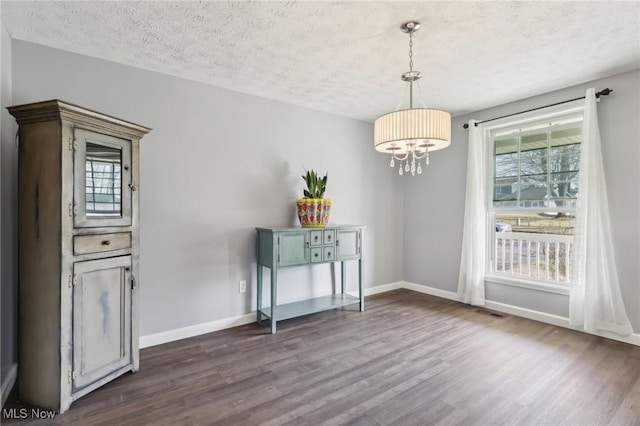 unfurnished dining area with dark wood-style floors, a notable chandelier, a textured ceiling, and baseboards