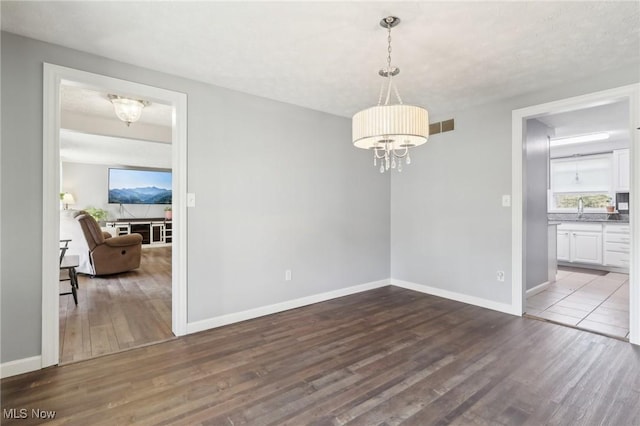 unfurnished dining area featuring wood finished floors, baseboards, visible vents, an inviting chandelier, and a sink