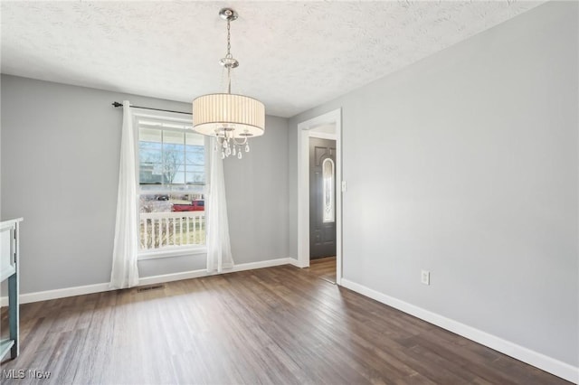 unfurnished dining area featuring baseboards, a notable chandelier, wood finished floors, and a textured ceiling