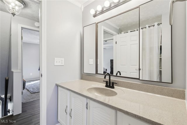 bathroom featuring wood finished floors, a textured ceiling, vanity, and ornamental molding