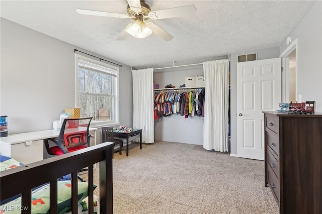 bedroom featuring a ceiling fan, visible vents, a closet, a textured ceiling, and light carpet