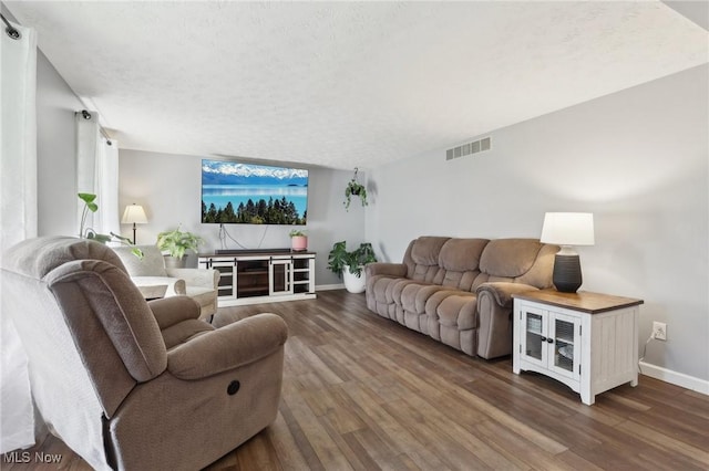 living room featuring baseboards, wood finished floors, visible vents, and a textured ceiling