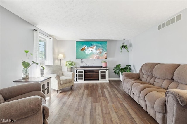 living area featuring baseboards, wood finished floors, visible vents, and a textured ceiling