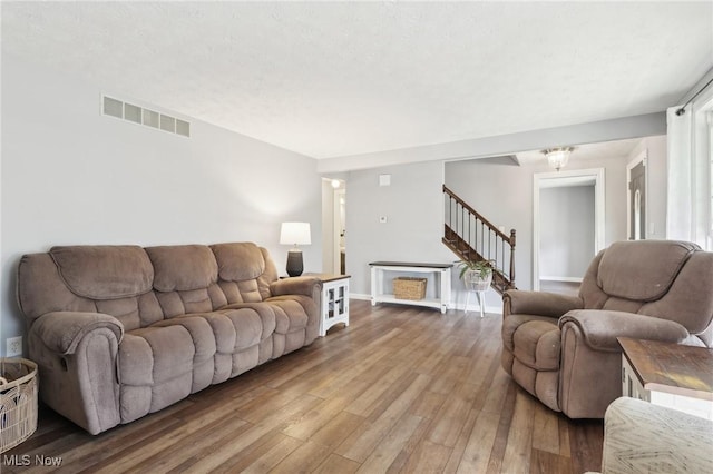 living area featuring visible vents, baseboards, wood finished floors, and stairs