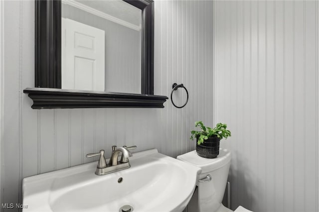 half bathroom with a sink, toilet, and ornamental molding