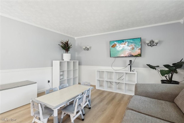 dining room featuring a textured ceiling, wood finished floors, wainscoting, and ornamental molding