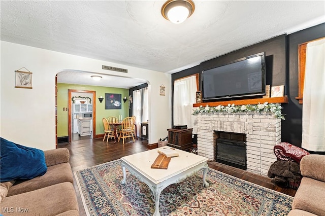 living room with visible vents, a textured ceiling, wood finished floors, arched walkways, and a fireplace