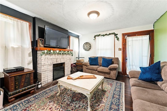 living area with a textured ceiling, a brick fireplace, and wood finished floors