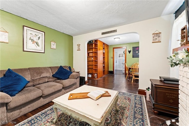 living area featuring visible vents, a textured ceiling, wood finished floors, arched walkways, and baseboards