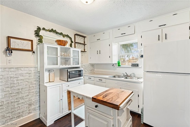 kitchen featuring a sink, stainless steel microwave, white cabinetry, and freestanding refrigerator