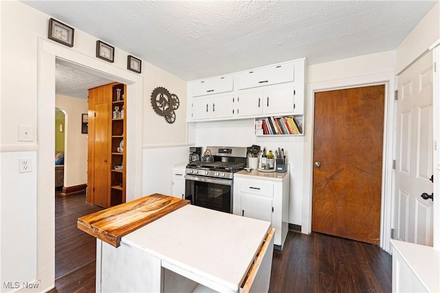 kitchen featuring stainless steel gas range, arched walkways, dark wood-type flooring, white cabinets, and light countertops