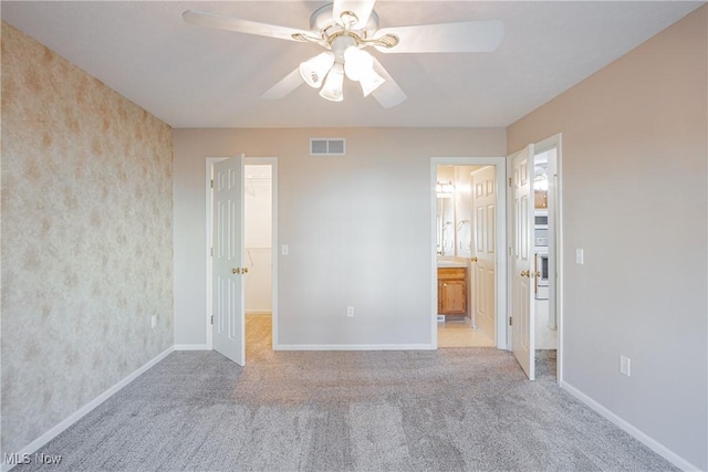 unfurnished bedroom featuring a spacious closet, visible vents, baseboards, carpet floors, and ensuite bath