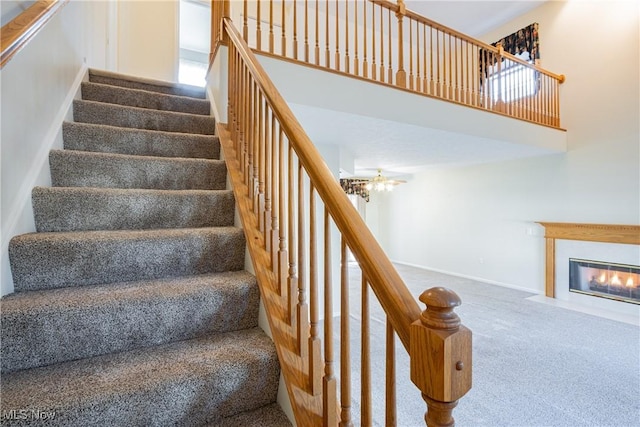 staircase featuring a fireplace with flush hearth, carpet flooring, baseboards, and a towering ceiling