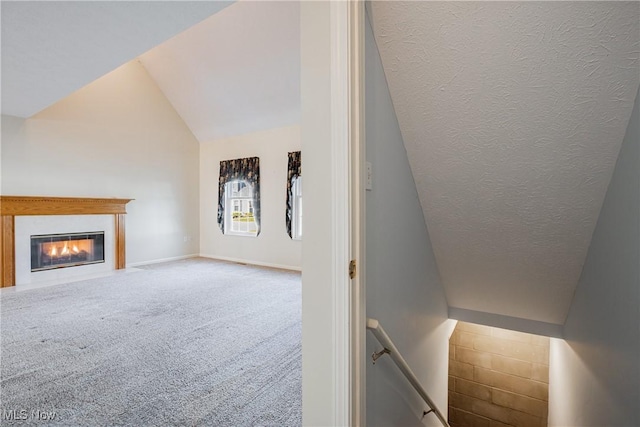 staircase with baseboards, carpet floors, vaulted ceiling, a textured ceiling, and a glass covered fireplace