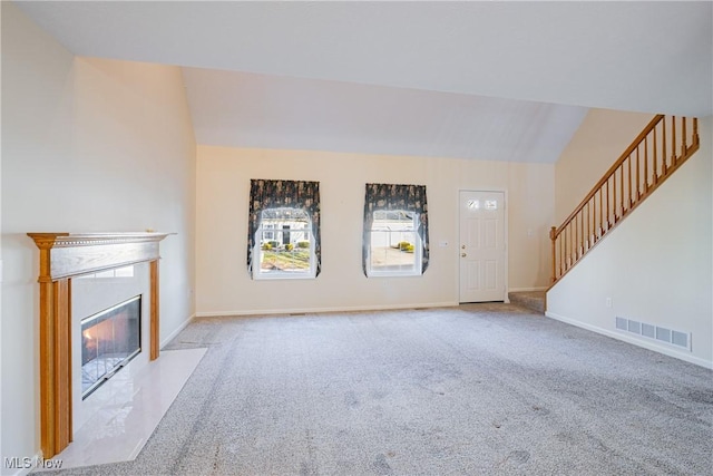 unfurnished living room featuring visible vents, a fireplace with flush hearth, carpet flooring, stairs, and vaulted ceiling