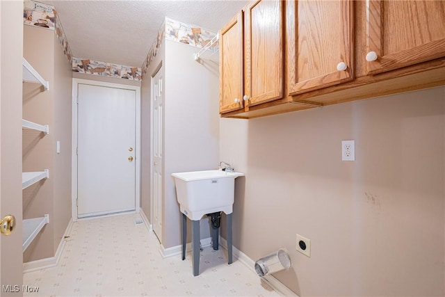 laundry area featuring light floors, baseboards, cabinet space, electric dryer hookup, and a textured ceiling