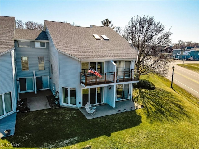 rear view of house featuring a balcony, a yard, a patio area, and a shingled roof