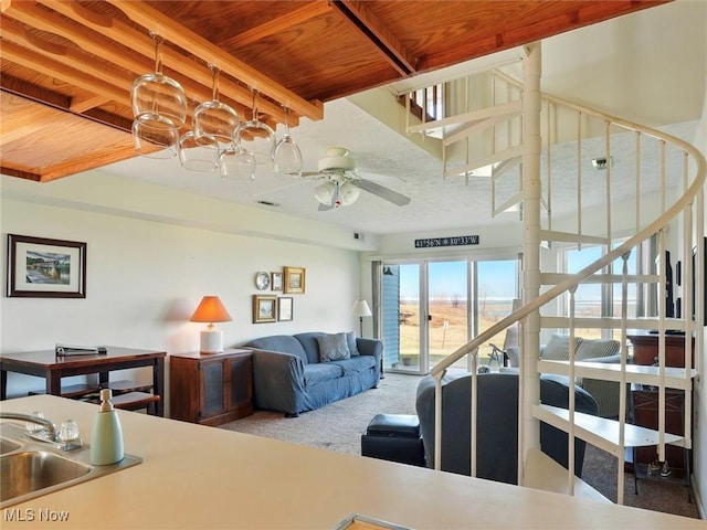 carpeted living area with stairway, visible vents, a sink, wood ceiling, and ceiling fan with notable chandelier