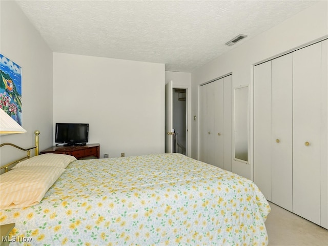 bedroom with light carpet, visible vents, multiple closets, and a textured ceiling