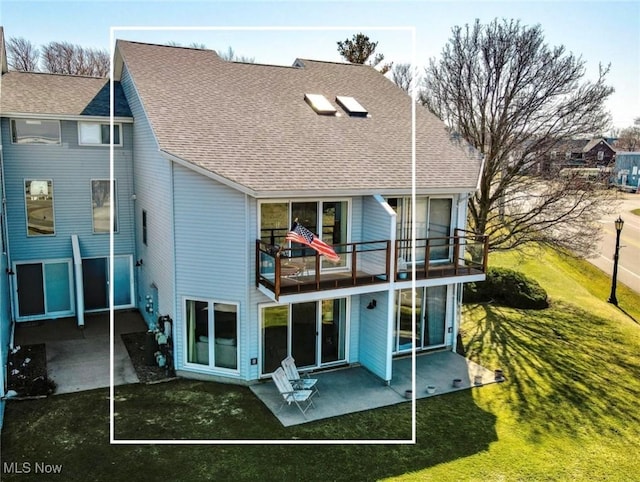 rear view of house featuring a yard, a patio, a balcony, and roof with shingles