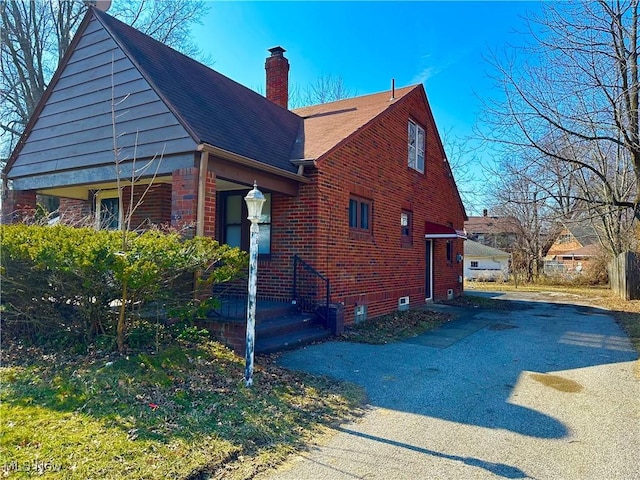 view of property exterior with brick siding, driveway, and a chimney