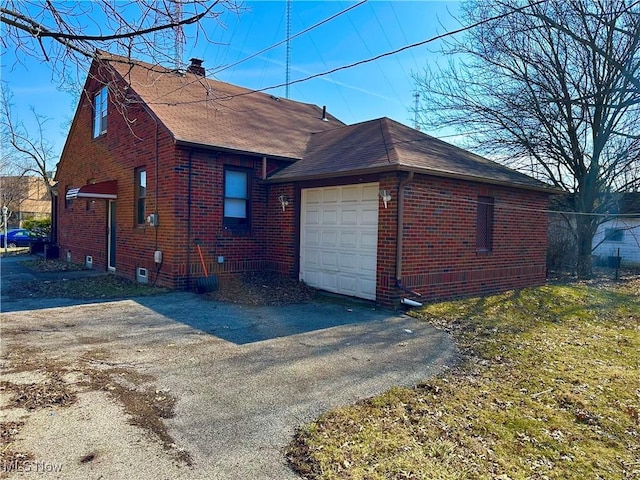 view of home's exterior with brick siding, an attached garage, a shingled roof, a chimney, and driveway