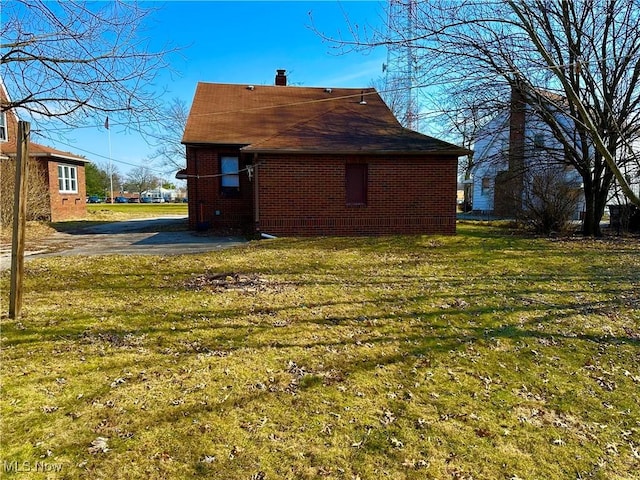 view of side of property featuring a yard, brick siding, and a chimney