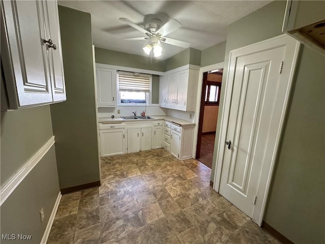 kitchen with white cabinetry, light countertops, a ceiling fan, and baseboards