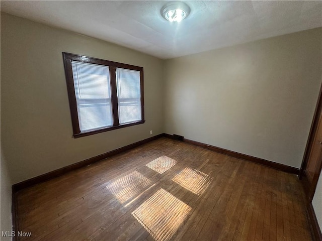 unfurnished room with baseboards and dark wood-style flooring