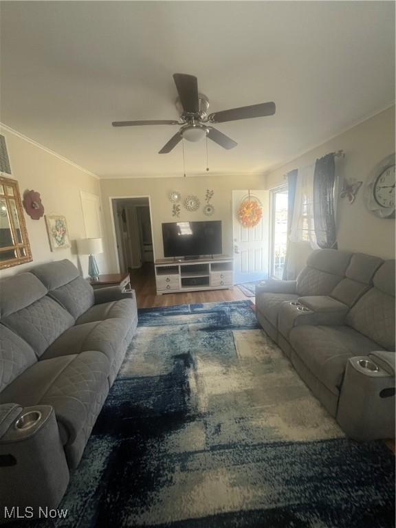 living area featuring wood finished floors, ceiling fan, and crown molding