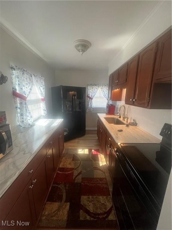 kitchen with a sink, black appliances, ornamental molding, and light countertops