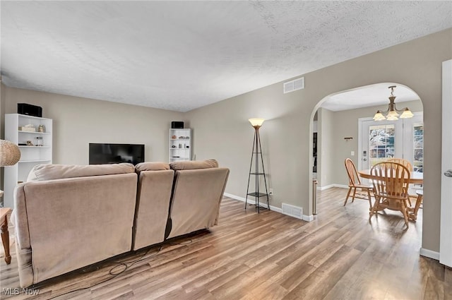 living room featuring arched walkways, visible vents, a chandelier, and wood finished floors