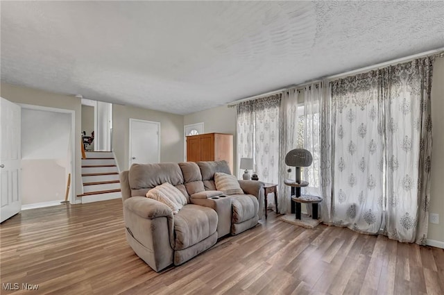 living room with stairs, light wood-style flooring, baseboards, and a textured ceiling