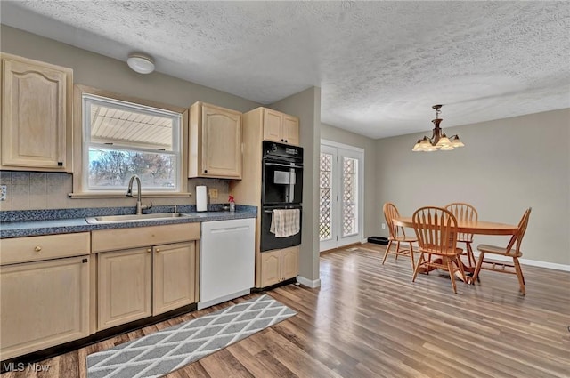 kitchen with white dishwasher, a sink, dark countertops, light wood-type flooring, and a chandelier