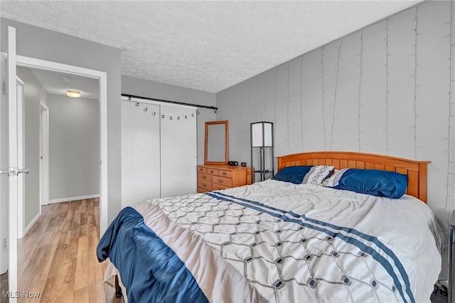 bedroom with a closet, baseboards, a textured ceiling, and wood finished floors