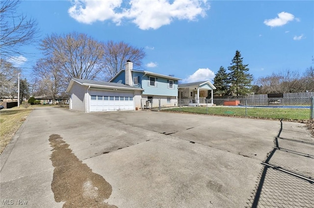 rear view of house featuring concrete driveway, fence, a garage, and a chimney