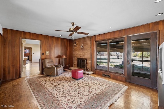 living area featuring wooden walls, plenty of natural light, visible vents, and ceiling fan