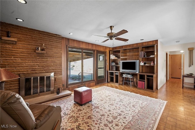 living area featuring built in shelves, a ceiling fan, a textured ceiling, recessed lighting, and wooden walls