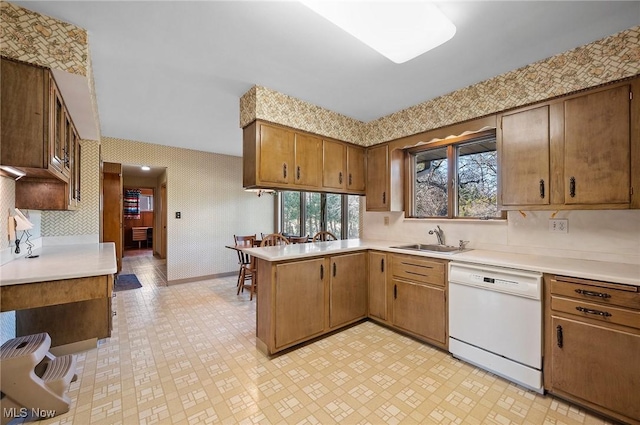 kitchen featuring a sink, wallpapered walls, a peninsula, light countertops, and dishwasher