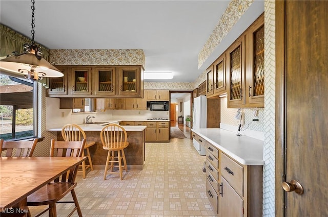 kitchen with wallpapered walls, a peninsula, light countertops, glass insert cabinets, and black microwave